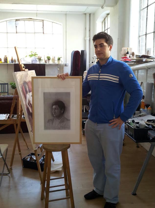Cristian beside a portrait drawing on an atelier easel